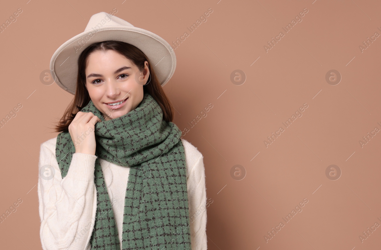 Photo of Beautiful woman in warm scarf and hat on brown background, space for text