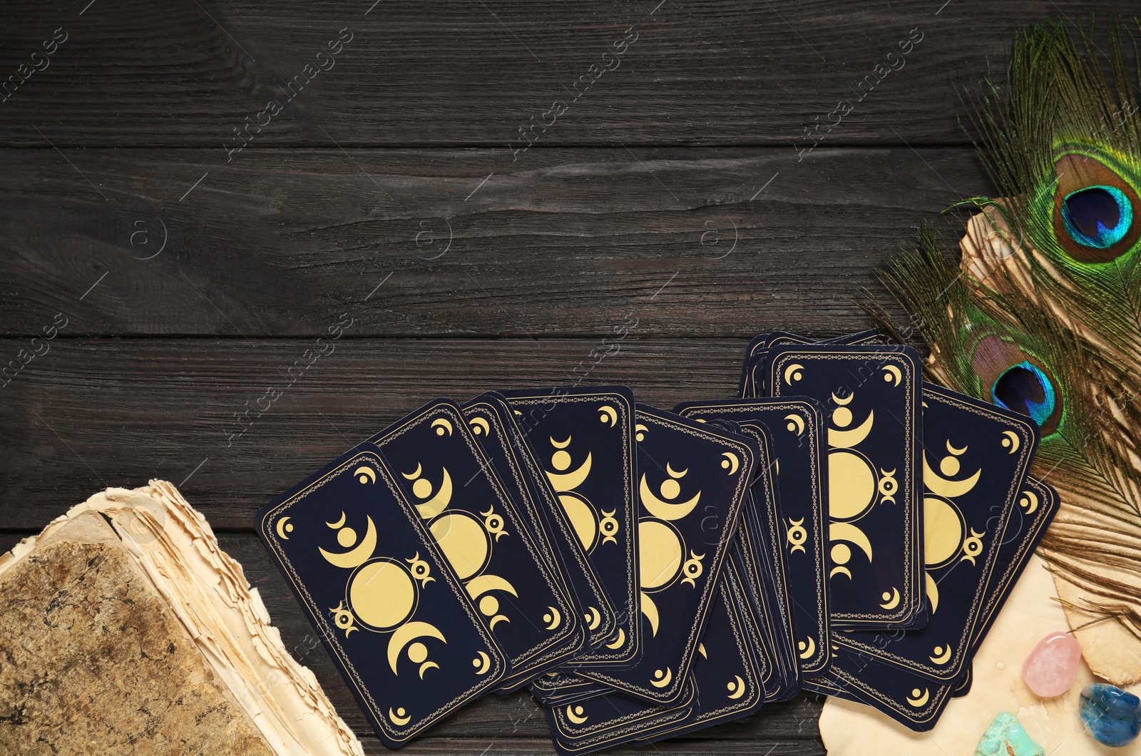 Photo of Tarot cards, peacock feathers, gemstones and old book on black wooden table, flat lay with space for text. Reverse side