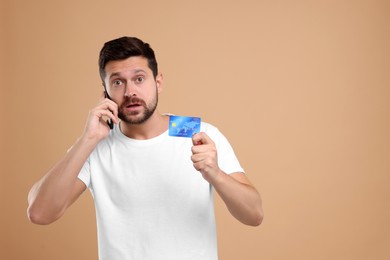 Photo of Shocked man with credit card talking on smartphone against beige background, space for text. Be careful - fraud