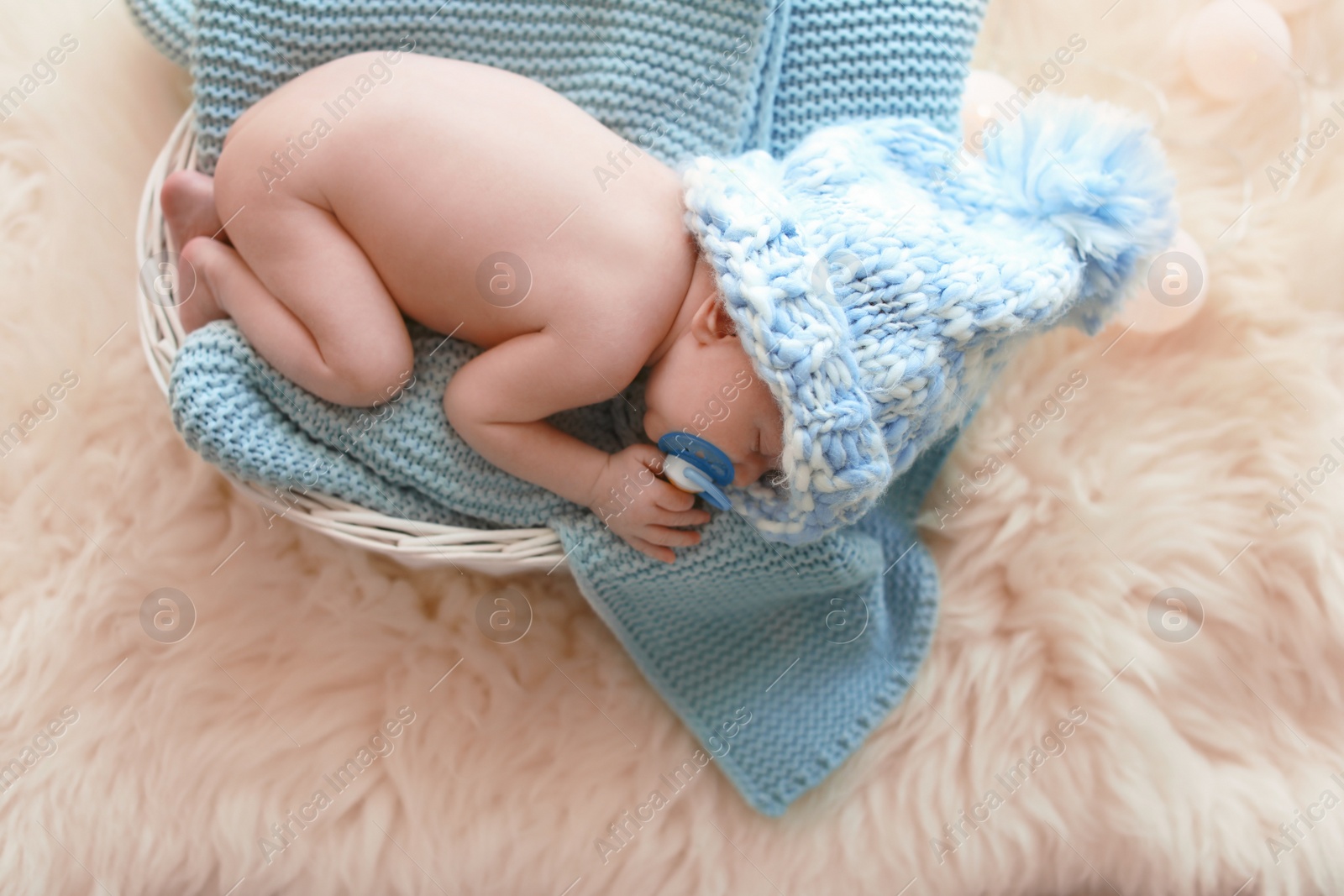 Photo of Adorable newborn baby lying in basket with knitted plaid on fuzzy rug, top view