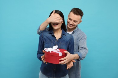 Photo of Boyfriend presenting gift to his girlfriend on light blue background