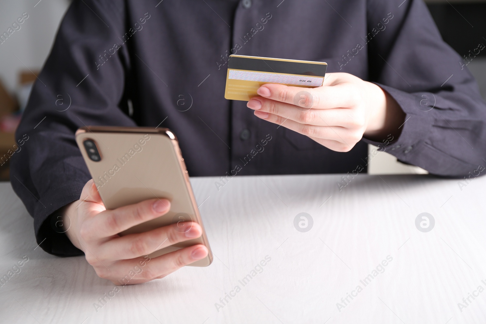 Photo of Online payment. Woman with smartphone and credit card at white wooden table, closeup