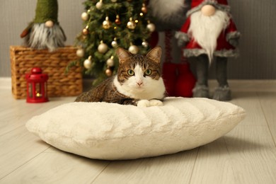 Photo of Cute cat lying on soft pillow near Christmas decor at home. Adorable pet