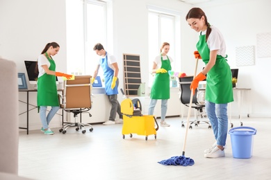 Team of professional janitors in uniform cleaning office