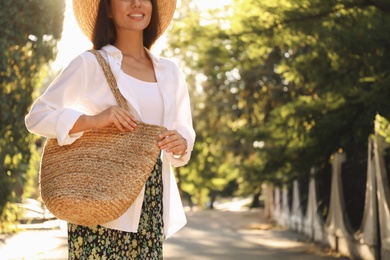 Photo of Young woman with stylish straw bag in park, closeup. Space for text