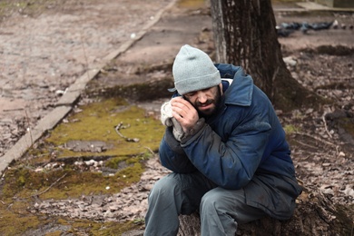 Poor homeless man sitting on stump outdoors