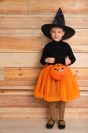 Photo of Cute little girl with pumpkin wearing Halloween costume near wooden wall