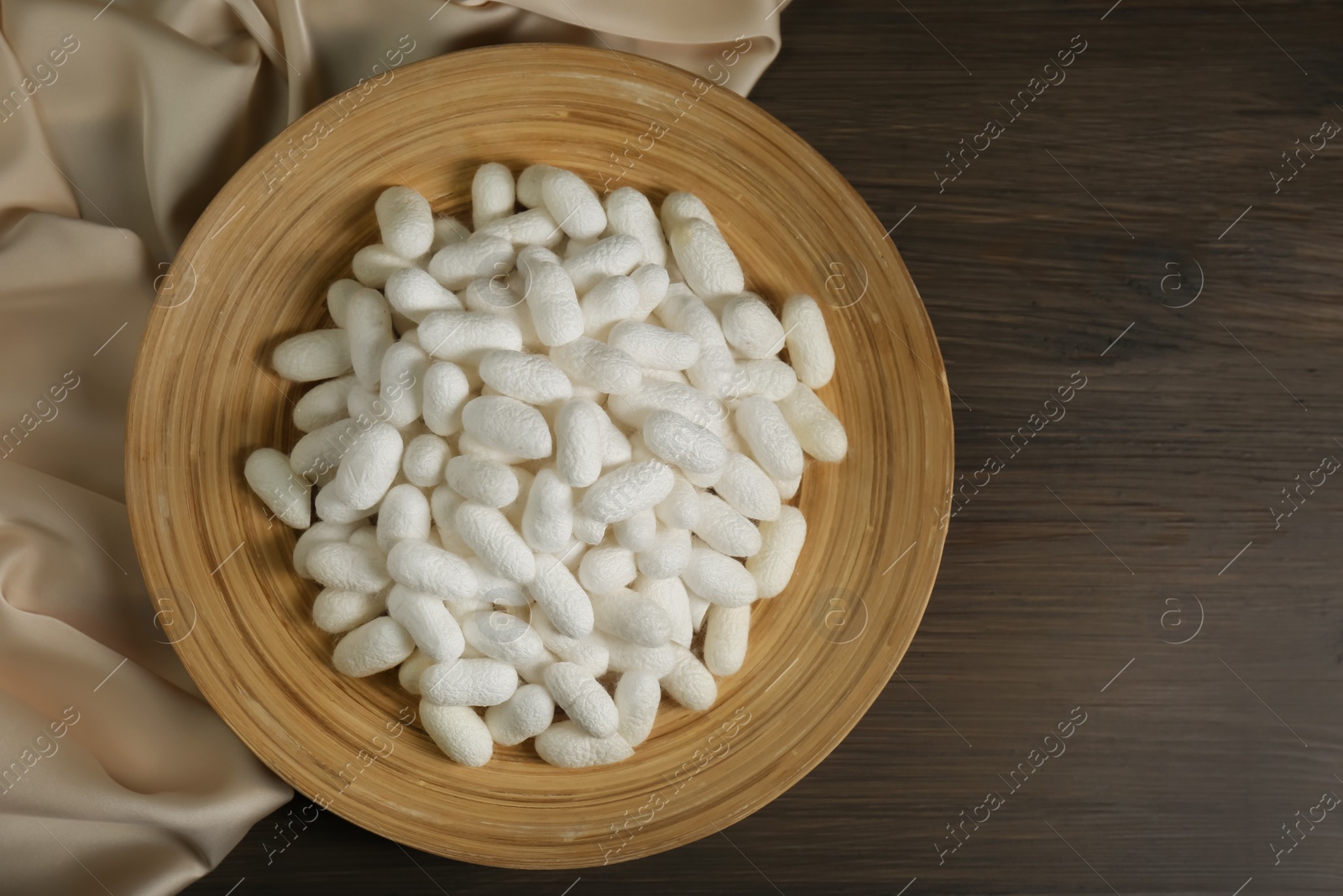 Photo of White cocoons with plate and silk fabric on wooden table, flat lay. Space for text