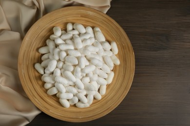 Photo of White cocoons with plate and silk fabric on wooden table, flat lay. Space for text