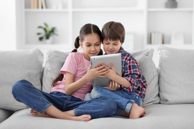 Happy brother and sister with tablet on sofa at home