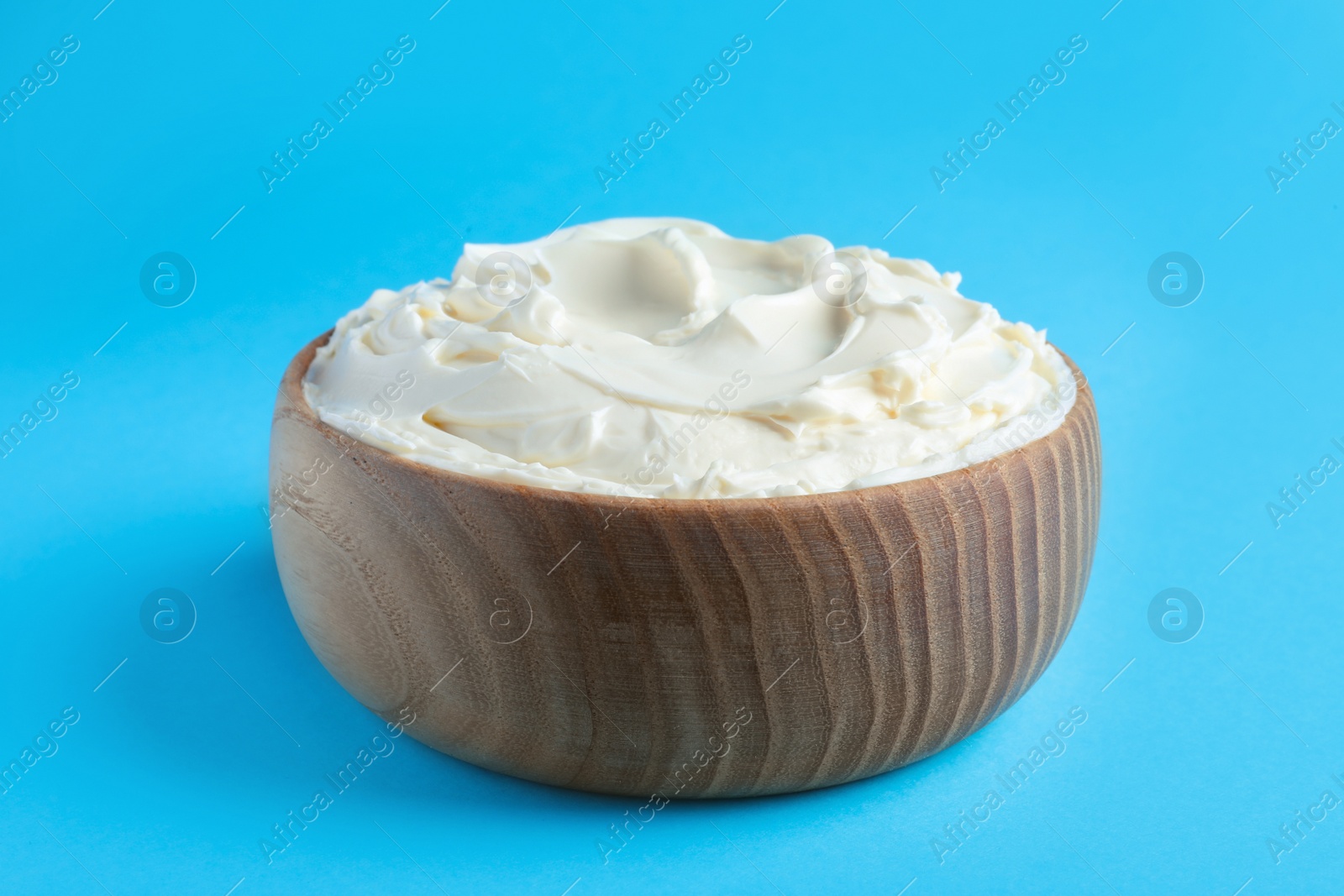 Photo of Bowl of tasty cream cheese on light blue background