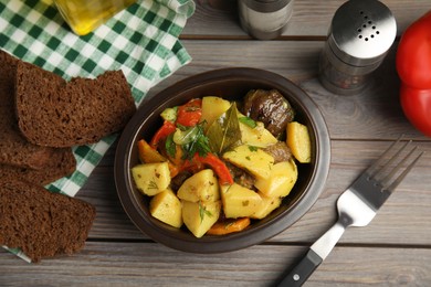 Tasty cooked dish with potatoes in earthenware served on wooden table, flat lay