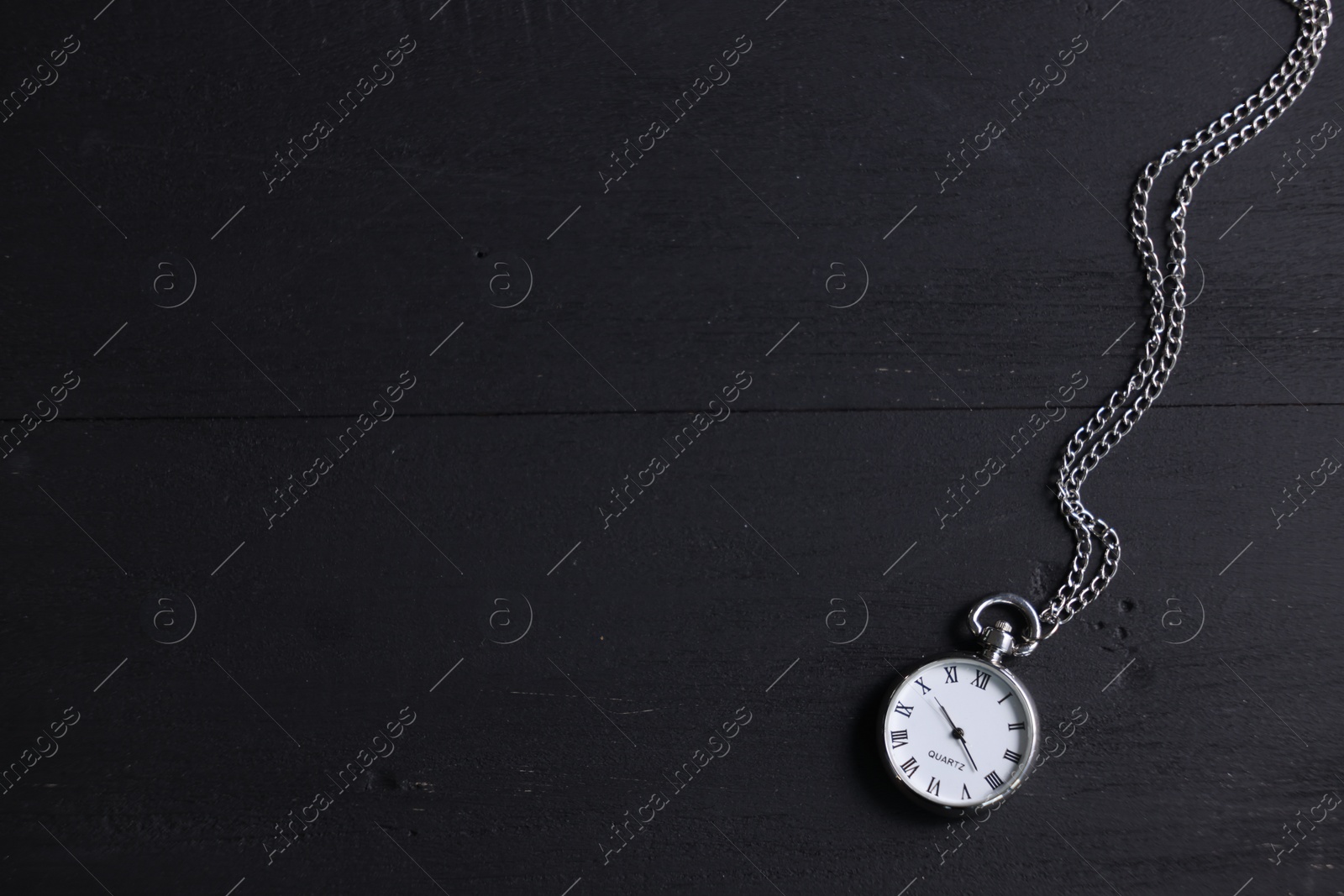 Photo of Silver pocket clock with chain on black wooden table, top view. Space for text