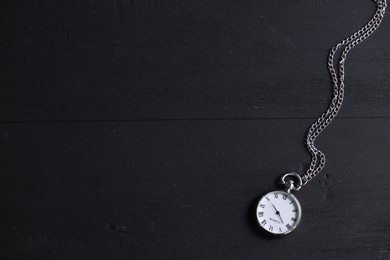 Silver pocket clock with chain on black wooden table, top view. Space for text