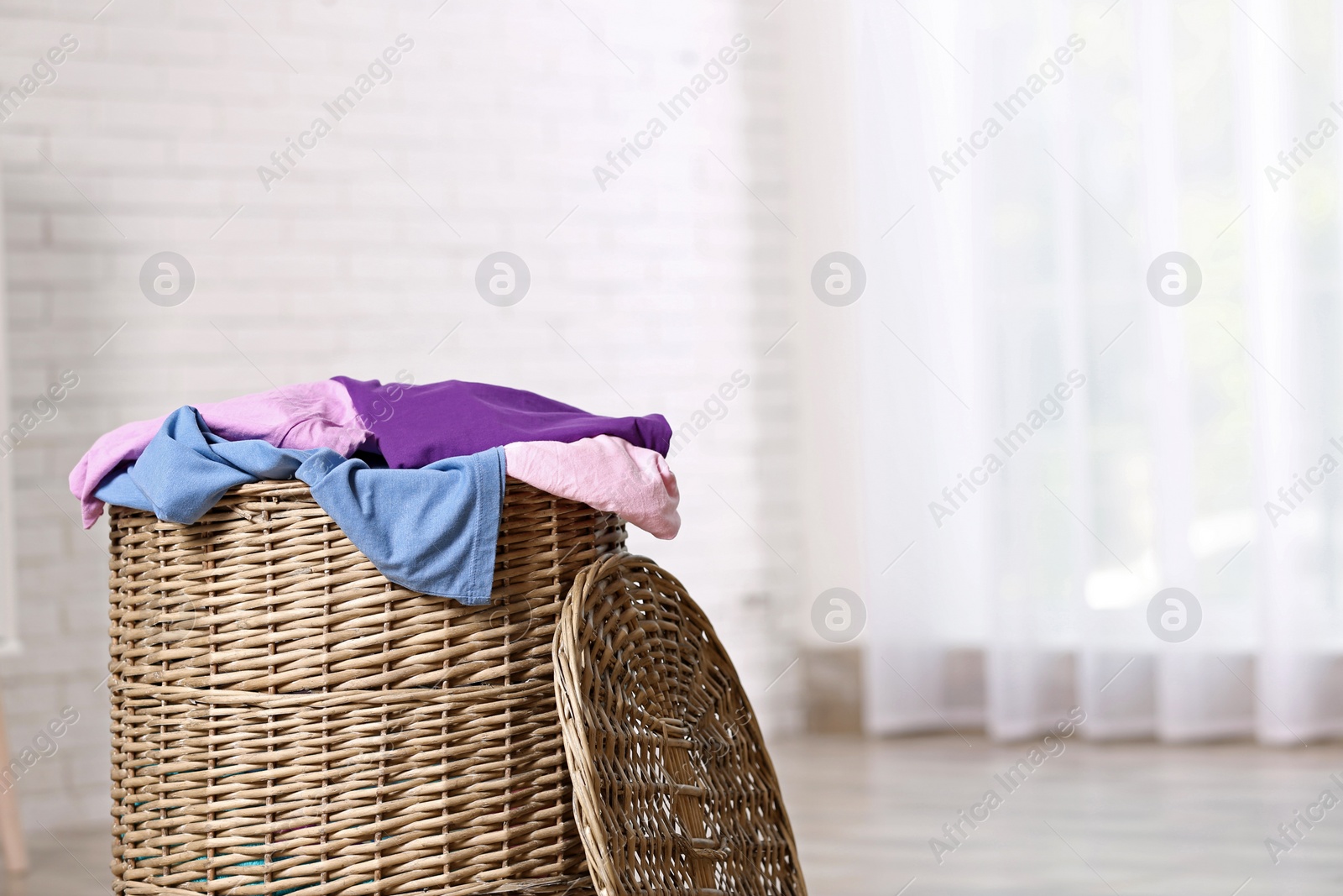 Photo of Wicker laundry basket with dirty clothes indoors. Space for text