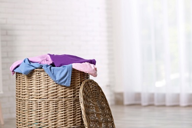 Photo of Wicker laundry basket with dirty clothes indoors. Space for text