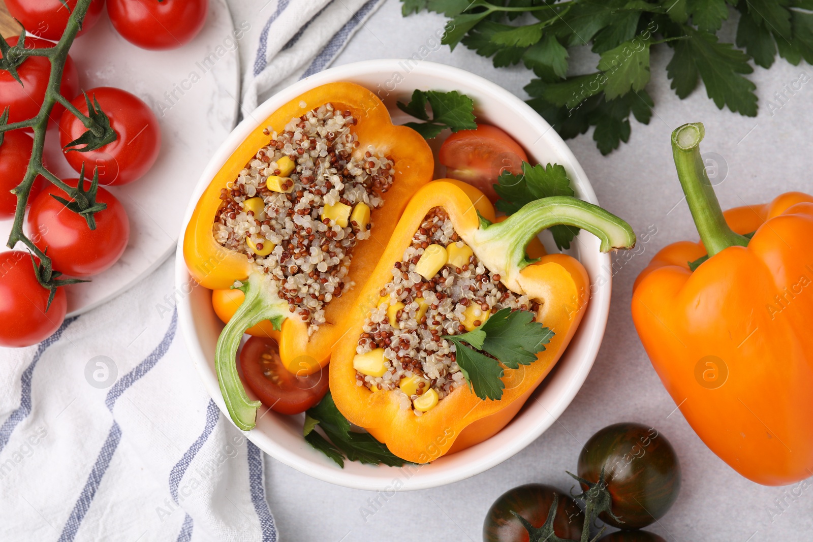 Photo of Quinoa stuffed bell pepper, tomatoes and parsley in bowl on light table, flat lay