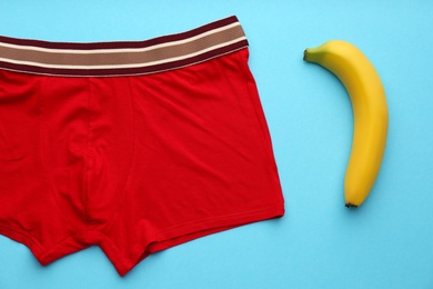 Men's underwear and banana on light blue background, flat lay. Potency problem concept