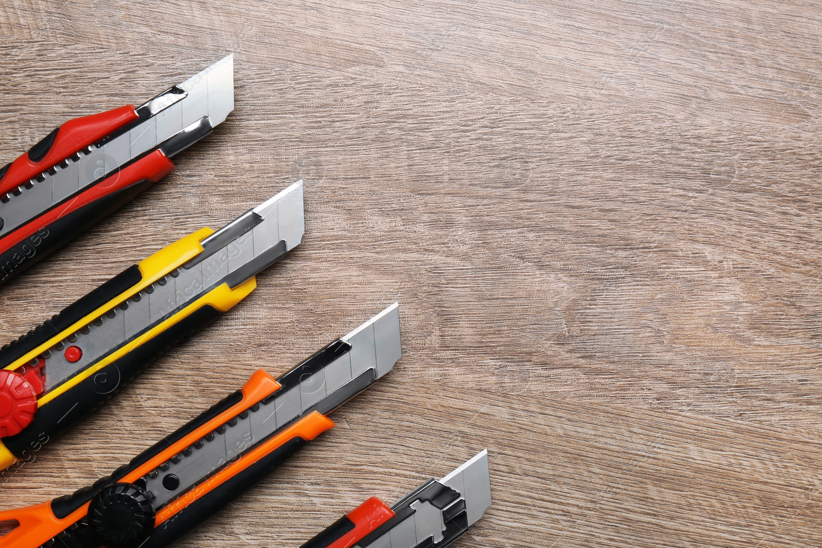 Photo of Many different utility knives on wooden table, flat lay. Space for text