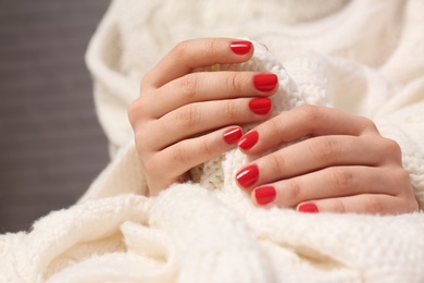 Woman with red manicure holding knitted fabric on blurred background, closeup. Nail polish trends