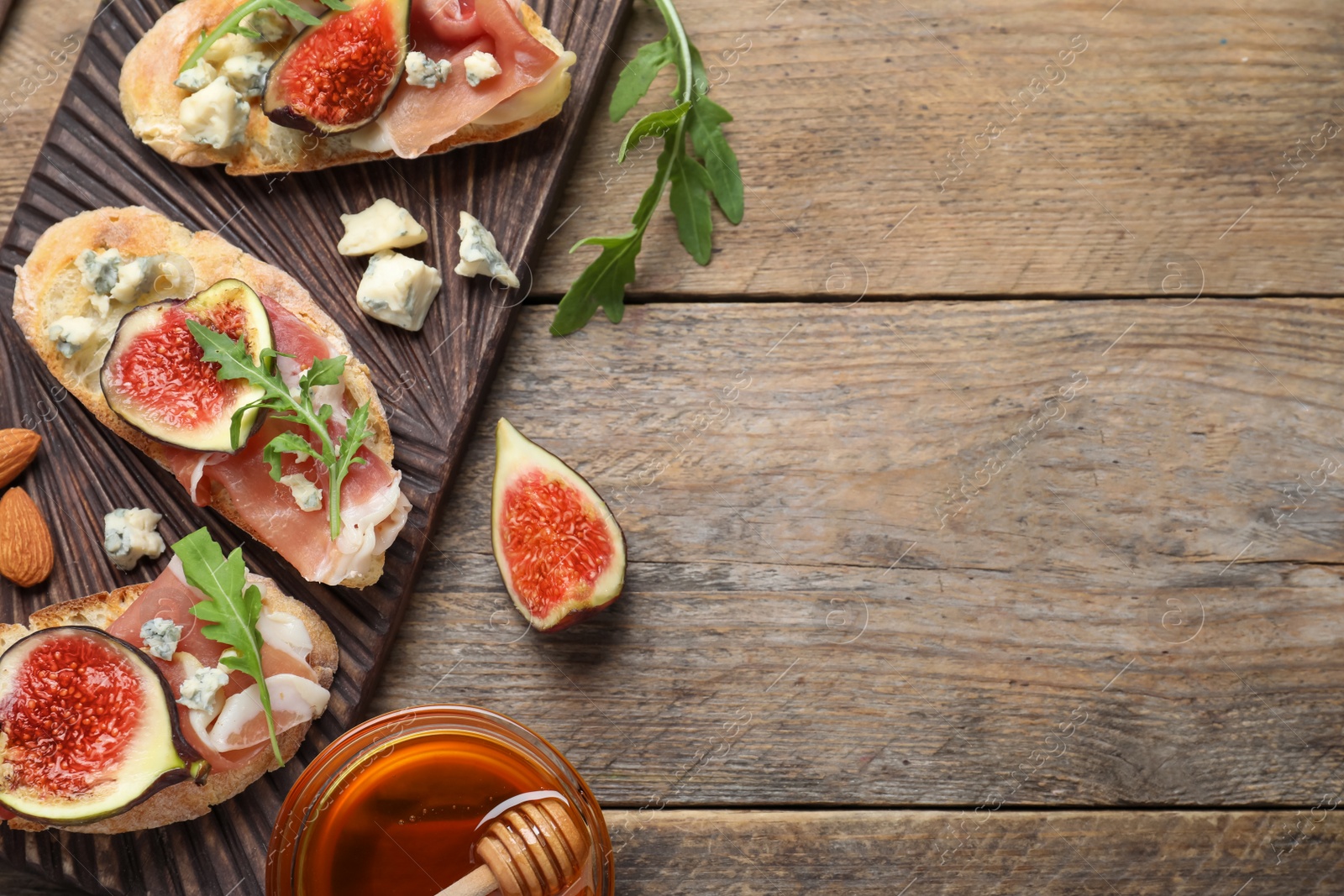 Photo of Sandwiches with ripe figs and prosciutto served on wooden table, flat lay. Space for text