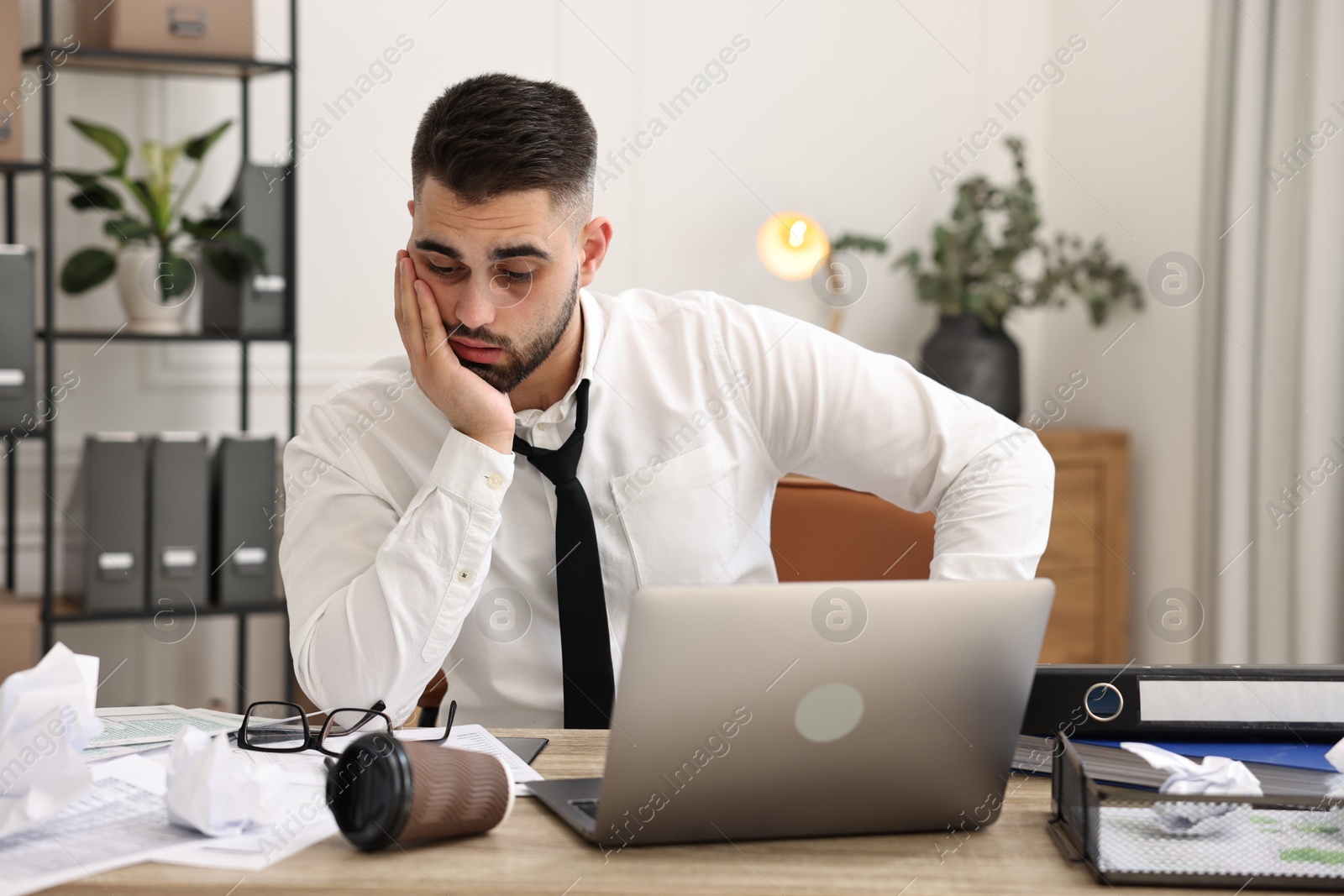 Photo of Overwhelmed man sitting at table with laptop and documents in office