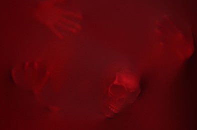 Silhouette of creepy ghost with skull behind red cloth