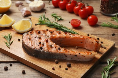 Photo of Tasty salmon steak with peppercorns, rosemary and lemon on wooden table