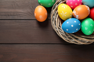 Photo of Colorful Easter eggs in decorative nest on wooden background, flat lay. Space for text