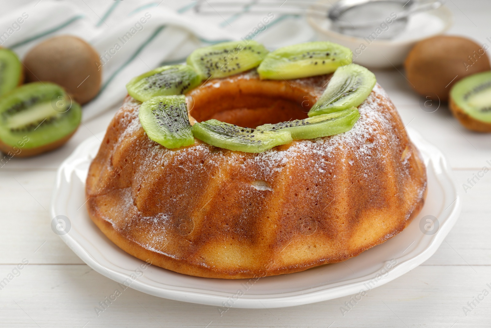 Photo of Homemade yogurt cake with kiwi and powdered sugar on white wooden table