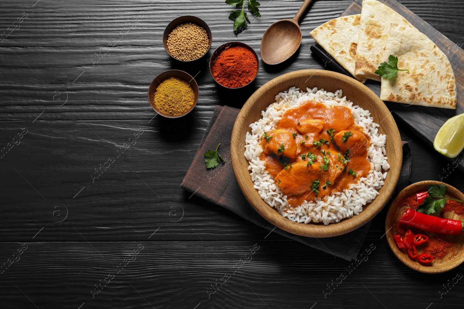 Photo of Delicious butter chicken with rice served on wooden table, flat lay. Space for text