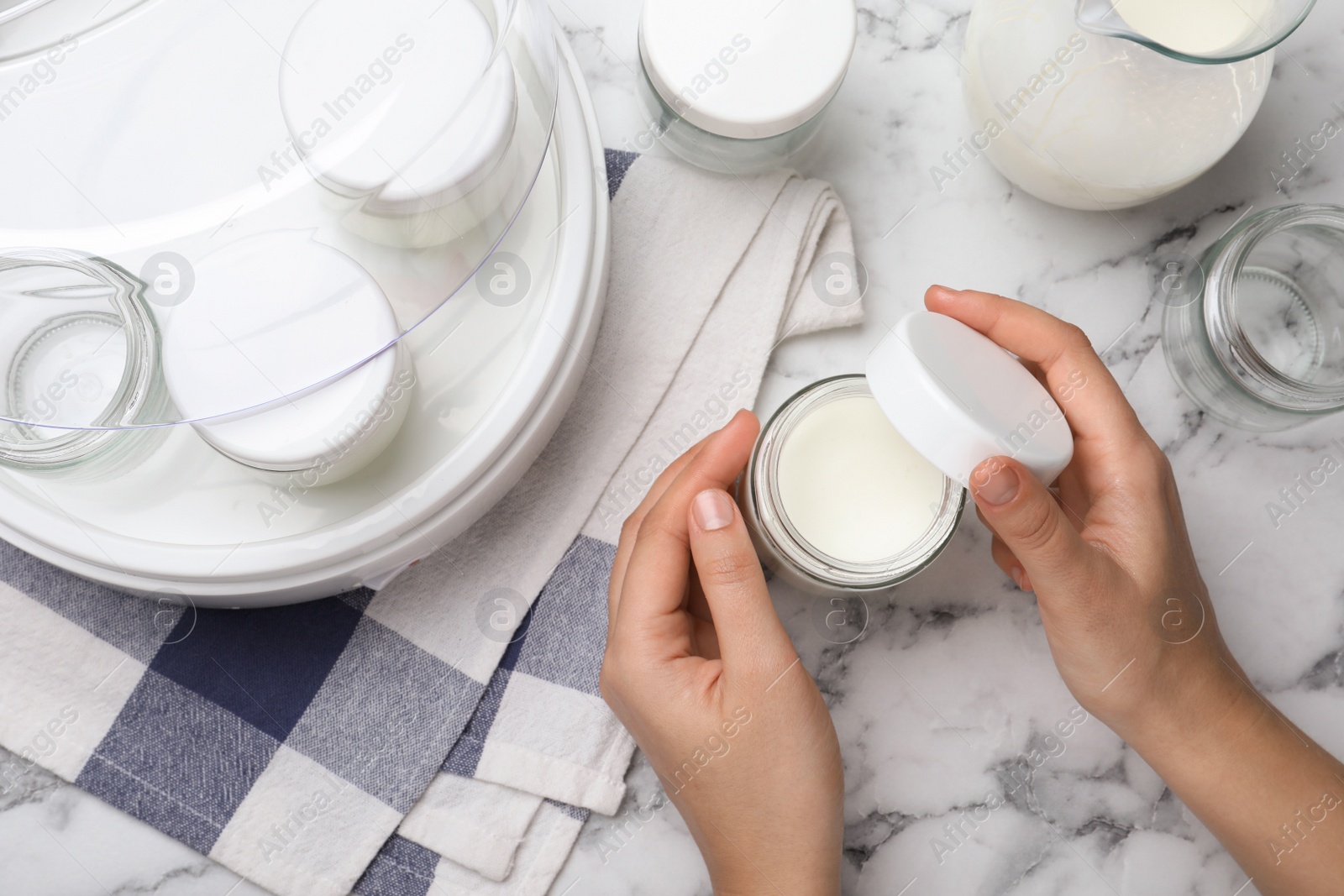 Photo of Woman with glass jar of tasty yogurt at white marble table, top view