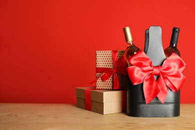 Photo of Bottles of wine in holder with bow and gift boxes on table against color background. Space for text