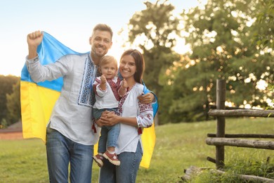 Photo of Happy cute family in embroidered national shirts with Ukrainian flag on sunny day. Space for text