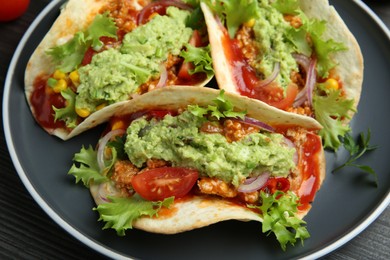 Delicious tacos with guacamole, meat and vegetables on table, closeup
