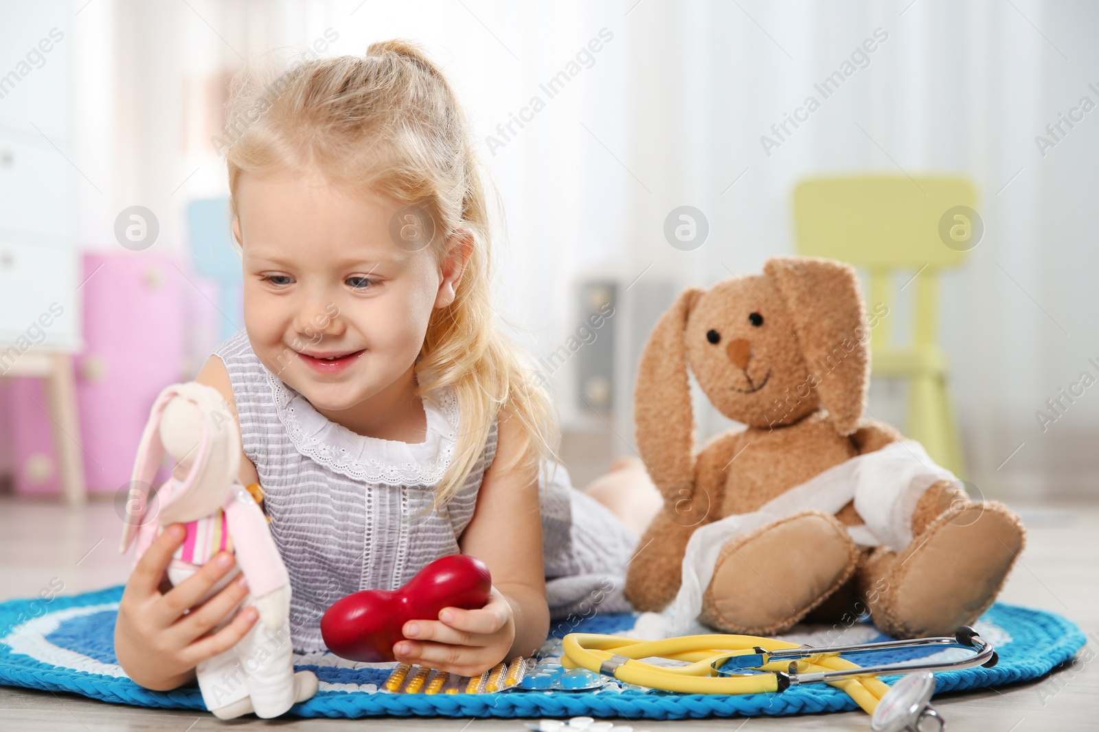 Photo of Cute child imagining herself as doctor while playing with toy bunny at home