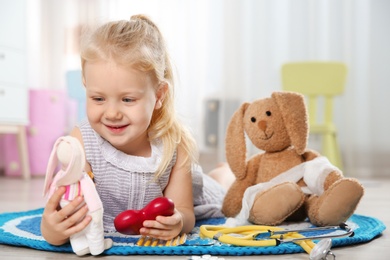 Cute child imagining herself as doctor while playing with toy bunny at home