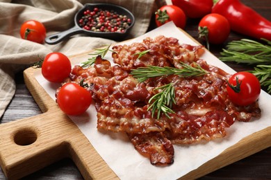 Photo of Slices of tasty fried bacon, rosemary, tomatoes and peppercorns on wooden table