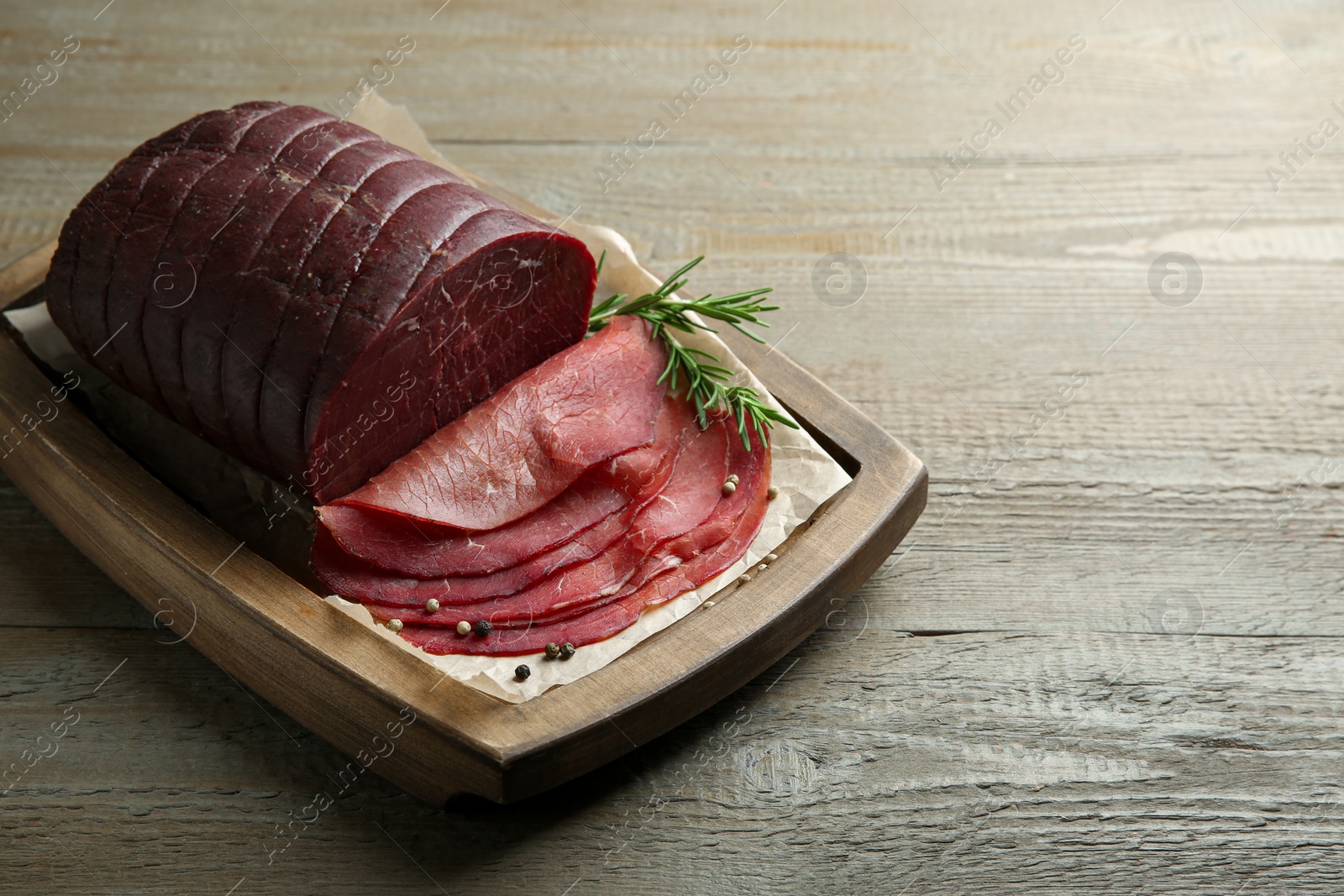 Photo of Tasty bresaola, peppercorns and rosemary on wooden table. Space for text