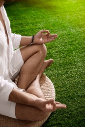 Young man meditating on straw cushion outdoors, closeup