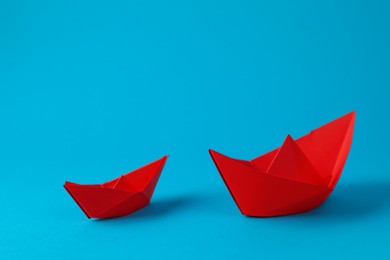 Photo of Two handmade red paper boats on light blue background. Origami art