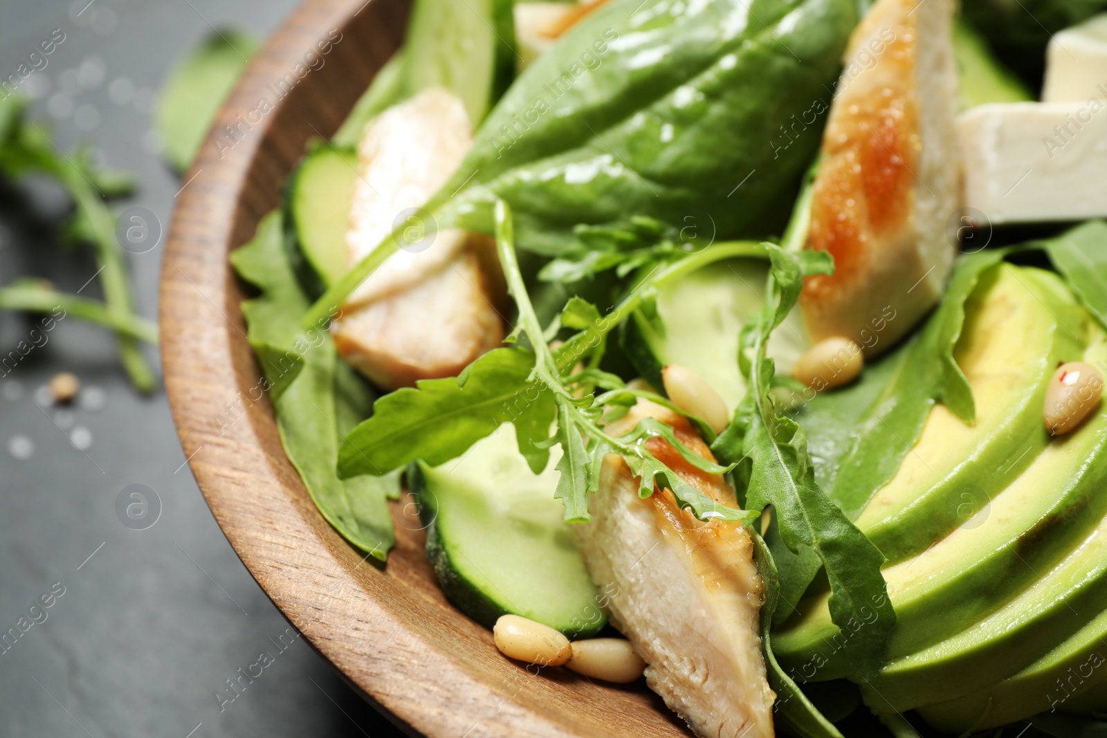 Photo of Delicious salad with chicken, arugula and avocado in bowl on table, closeup