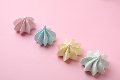 Many tasty meringue cookies on pink background