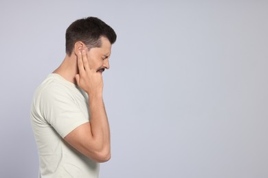 Photo of Man suffering from ear pain on grey background, space for text