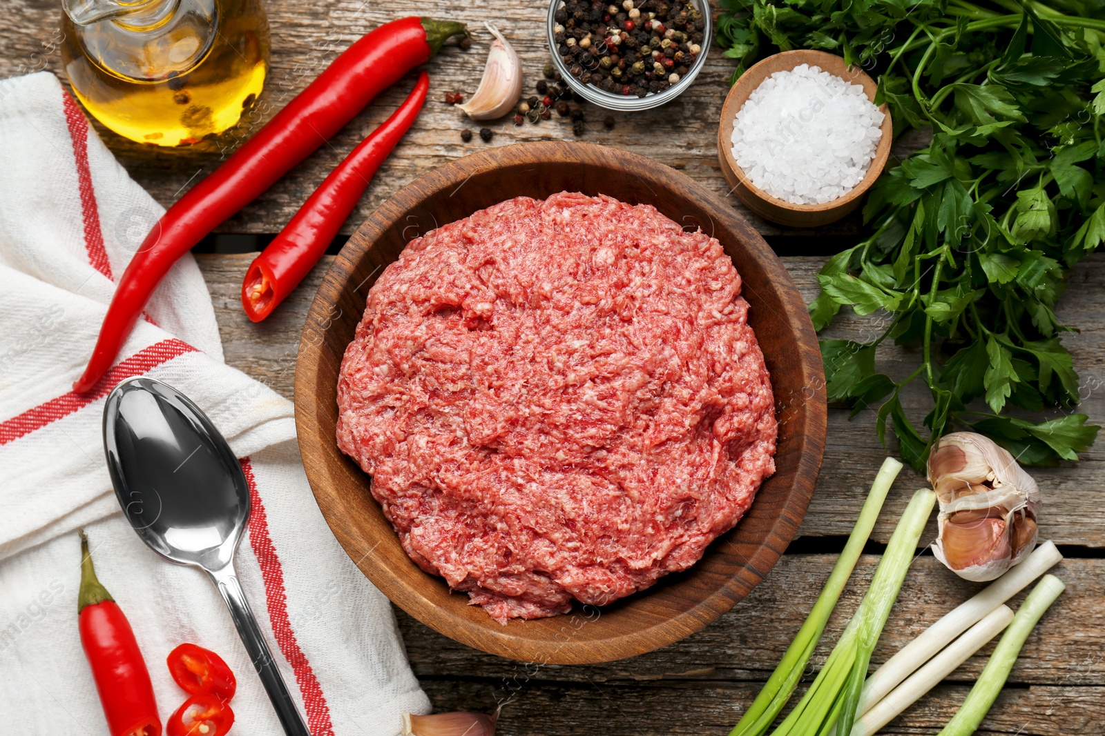 Photo of Bowl with raw fresh minced meat and ingredients on wooden table, flat lay