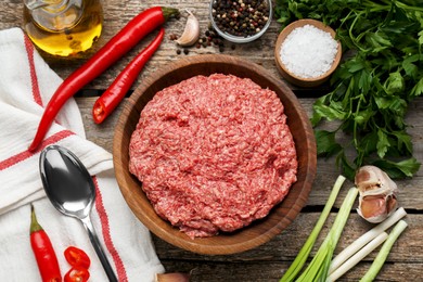 Bowl with raw fresh minced meat and ingredients on wooden table, flat lay