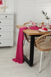 Photo of Color accent table setting. Glasses, plates, pink napkins and vase with green branch in dining room