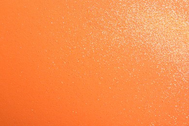 Photo of Shiny bright glitter on orange background, flat lay. Space for text