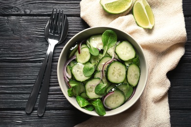 Photo of Delicious cucumber salad with onion and spinach in bowl served on wooden table, top view