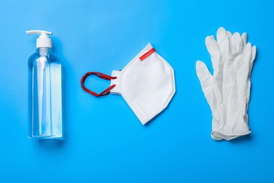 Medical gloves, respiratory mask and hand sanitizer on light blue background, flat lay
